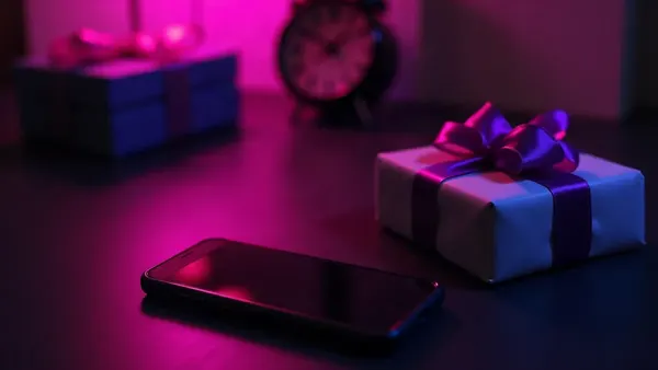 Smartphone junto a un pequeño regalo con lazo violeta, en un escritorio oscuro (ilustración del artículo)
